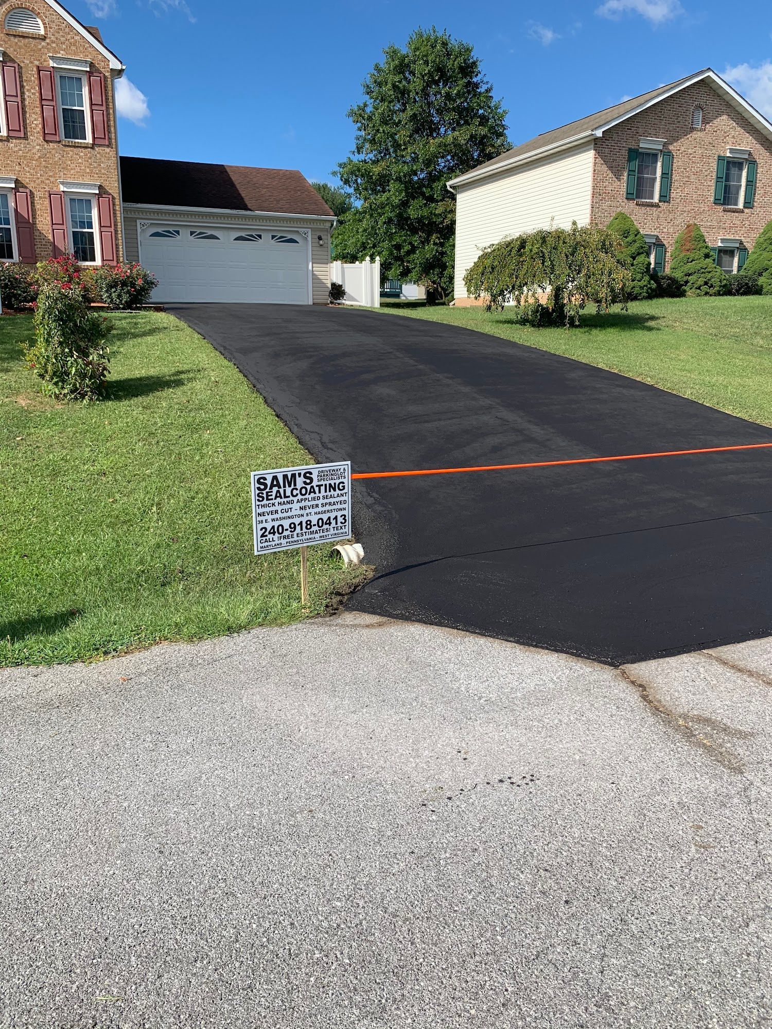 Residential driveway freshly paved between two brick houses, with a small sign at the edge.