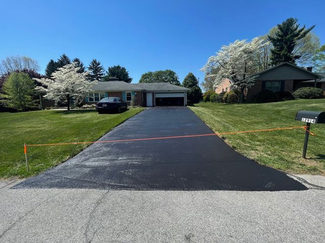 Long asphalt driveway leading to a single-story house with a parked car and spring trees under a blue sky