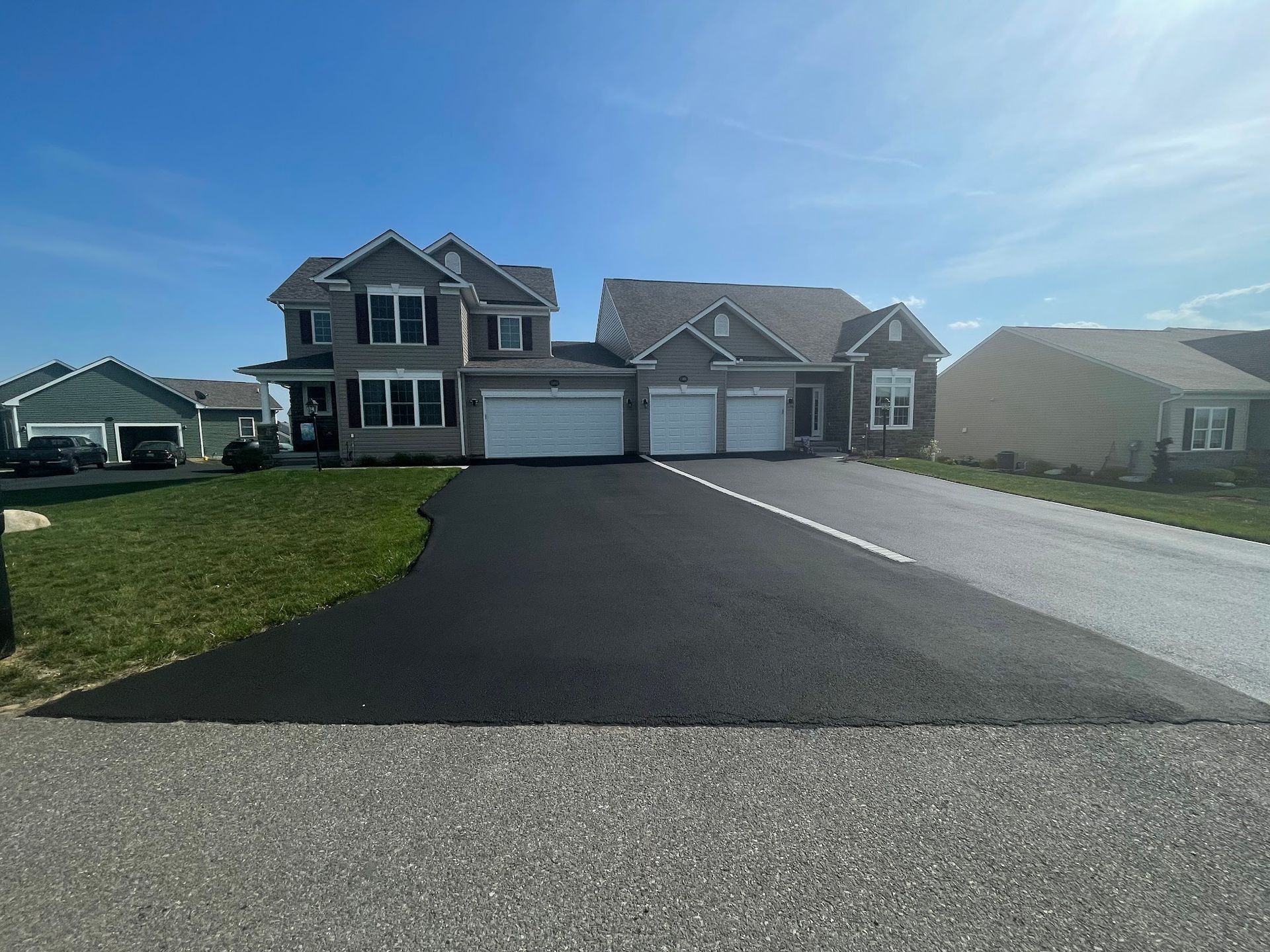 Suburban house with a long black driveway under a bright blue sky
