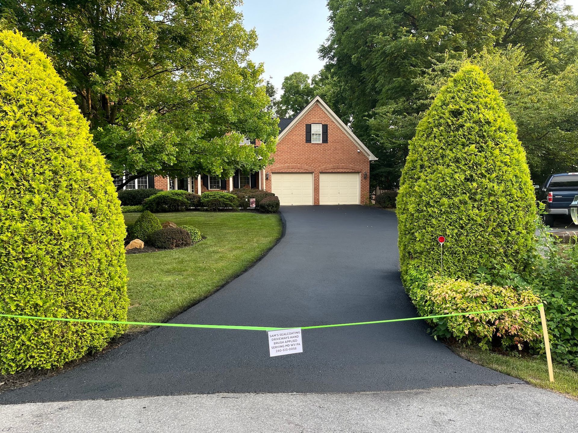 Driveway blocked by green tape, leading to a brick house with a two-car garage and manicured shrubs.