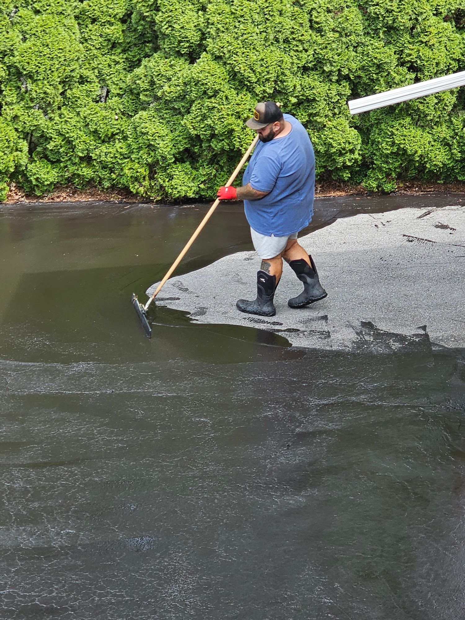 Person in a blue shirt and red gloves fishing with a net from a muddy riverbank.