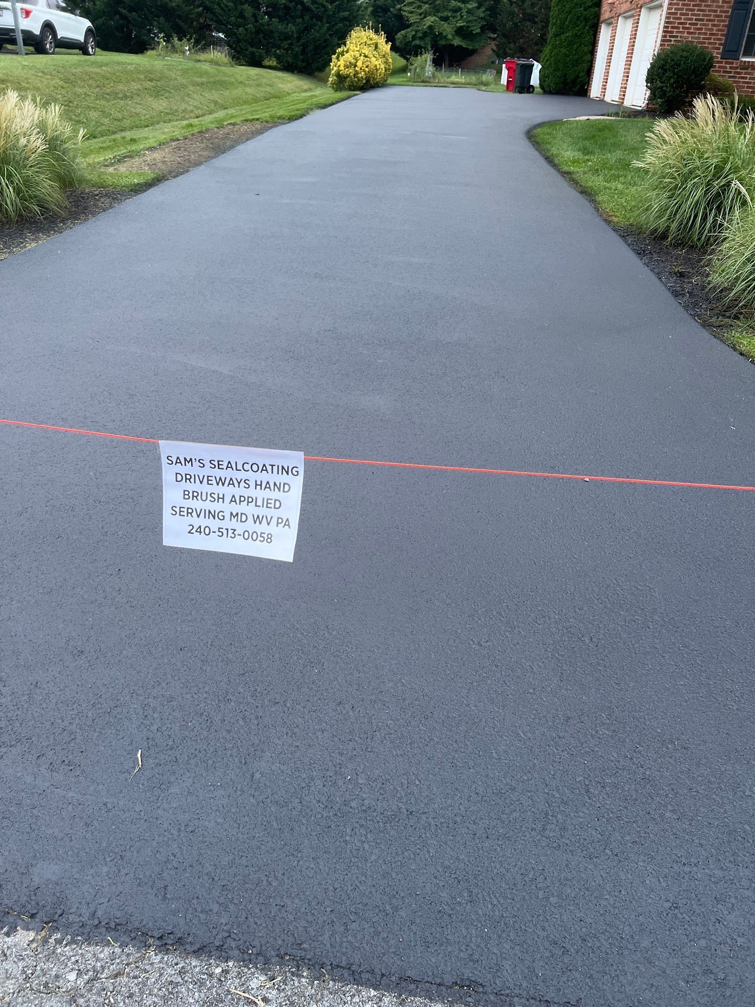 Asphalt driveway cordoned off with red tape and a small warning sign near a house