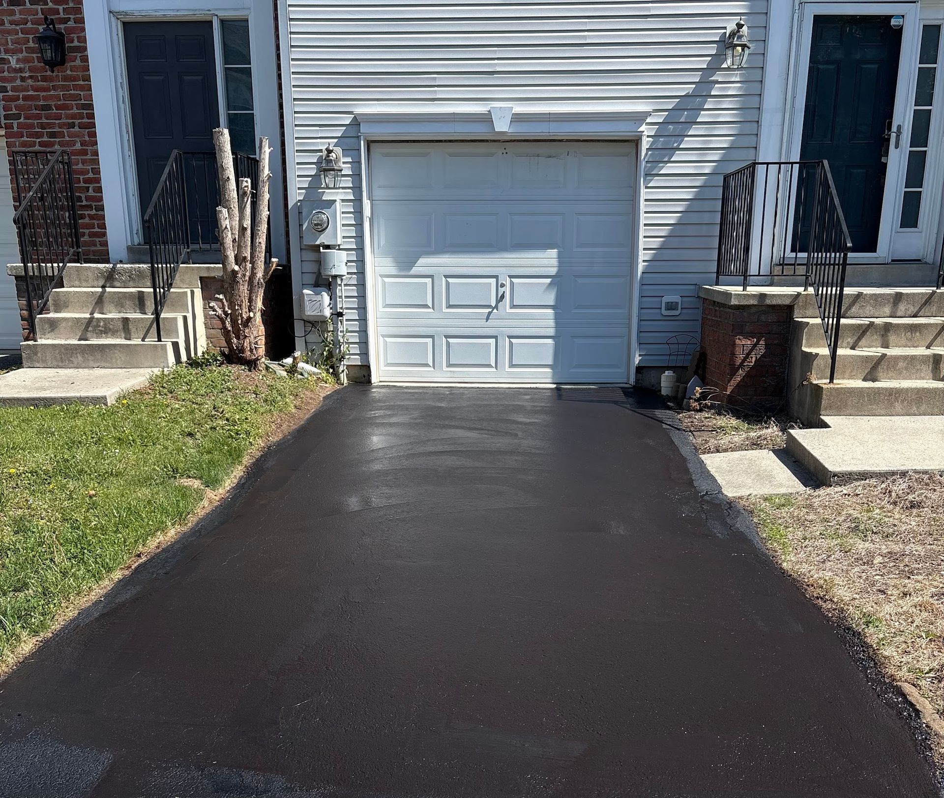 Fresh black driveway leading to a white garage door on a house exterior