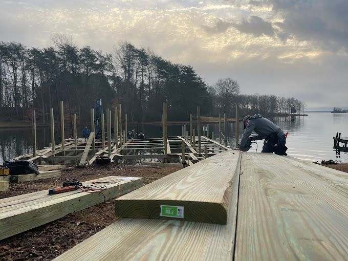 A man is working on a wooden dock next to a lake.