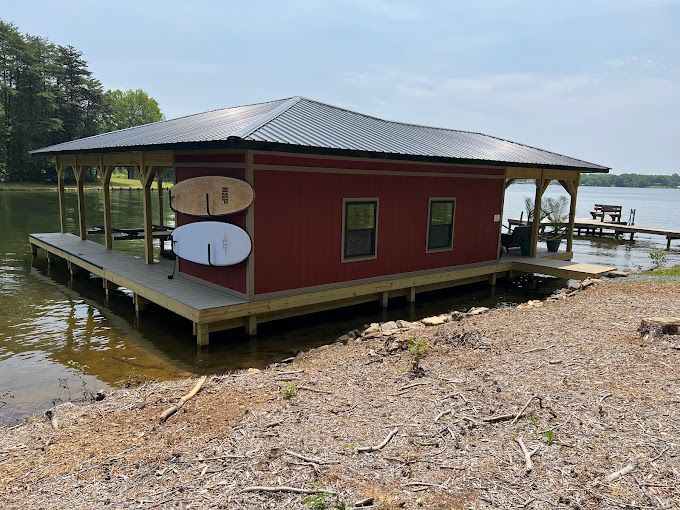 A red house is sitting on top of a wooden dock next to a lake.