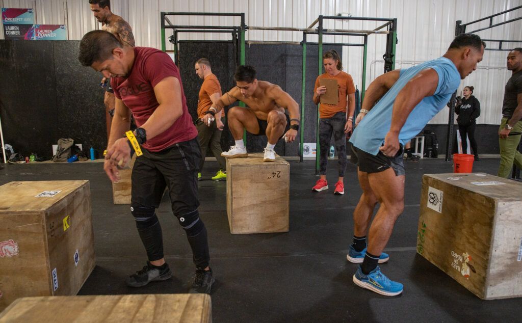 A group of men are jumping over wooden boxes in a gym.
