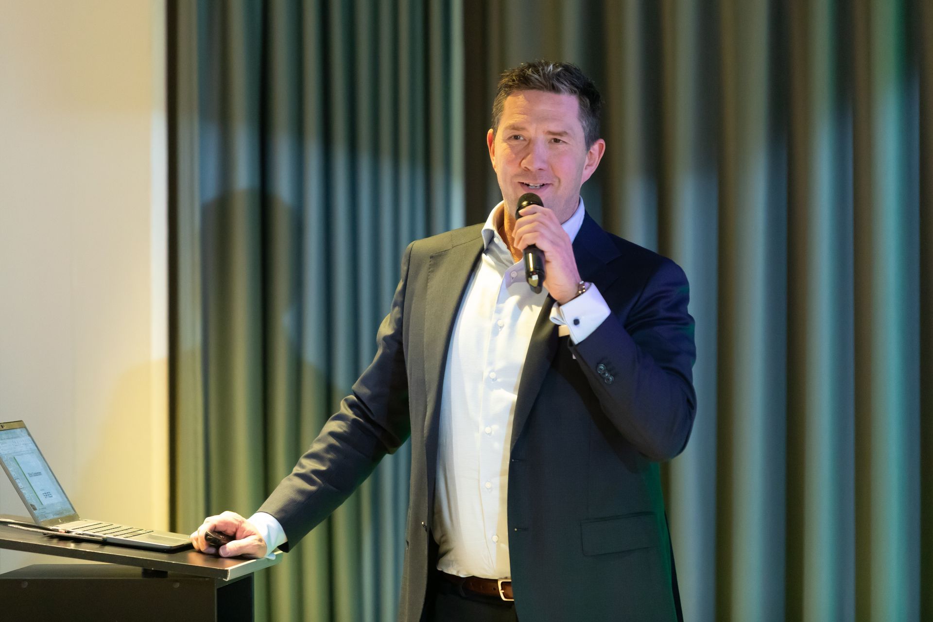 Ein Mann im Anzug steht an einem Podium und hält ein Mikrofon.
