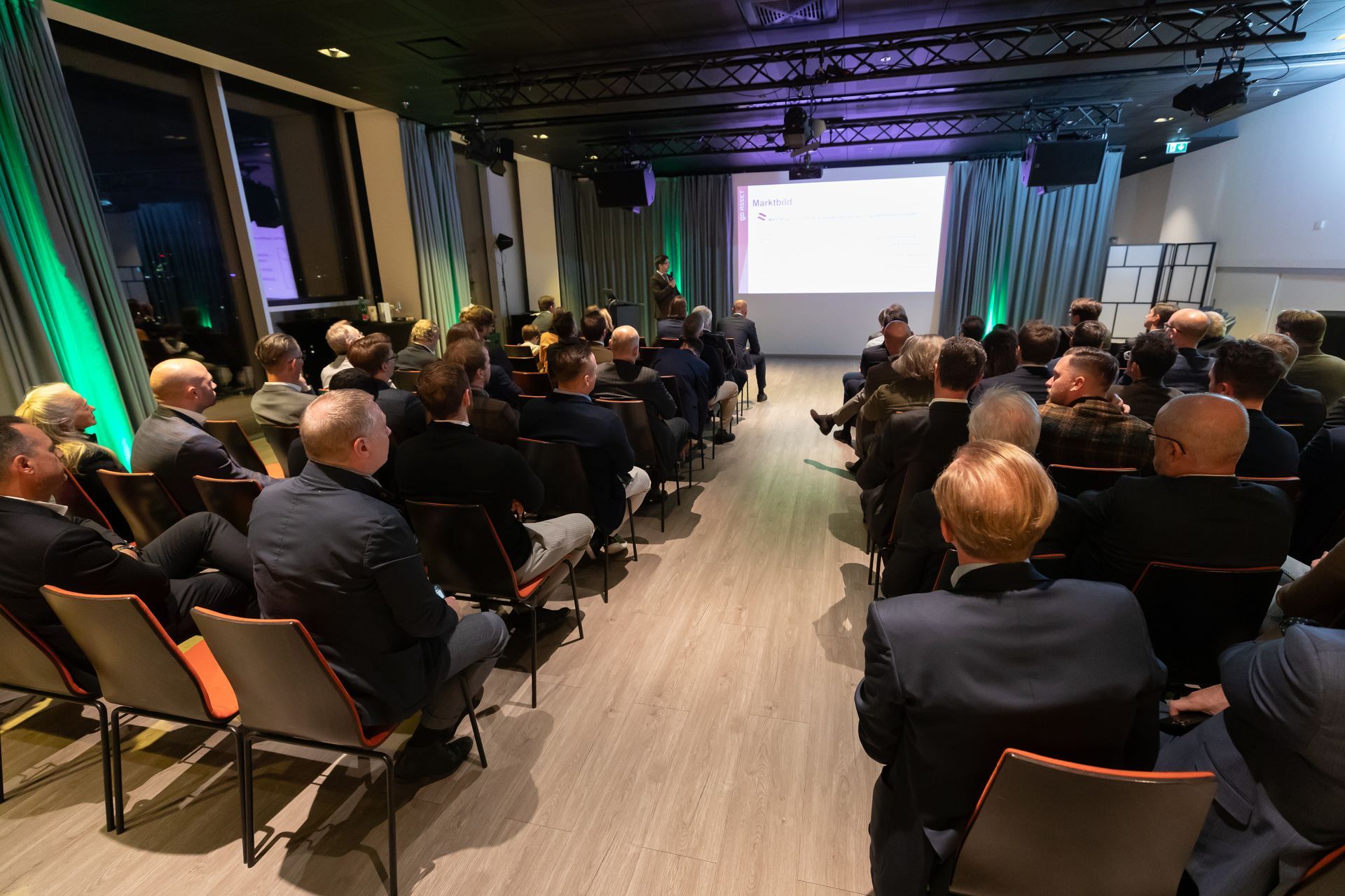 Eine große Gruppe von Menschen sitzt in einem Konferenzraum und sieht sich eine Präsentation an.