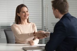 Two people shaking hands across a desk in a bright office
