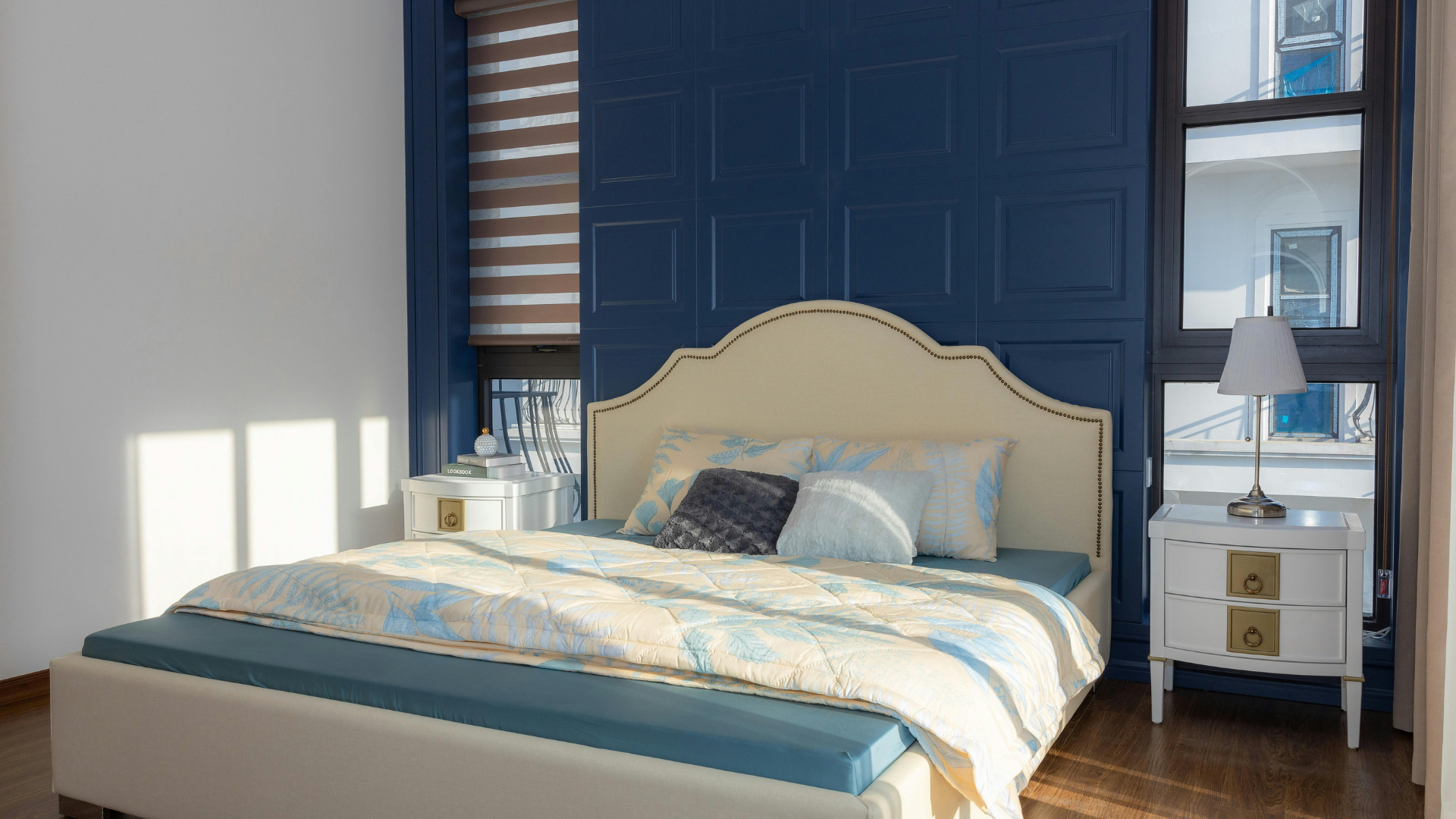 Bright bedroom with cream bedspread, navy accent wall, and white nightstands by a sunlit window