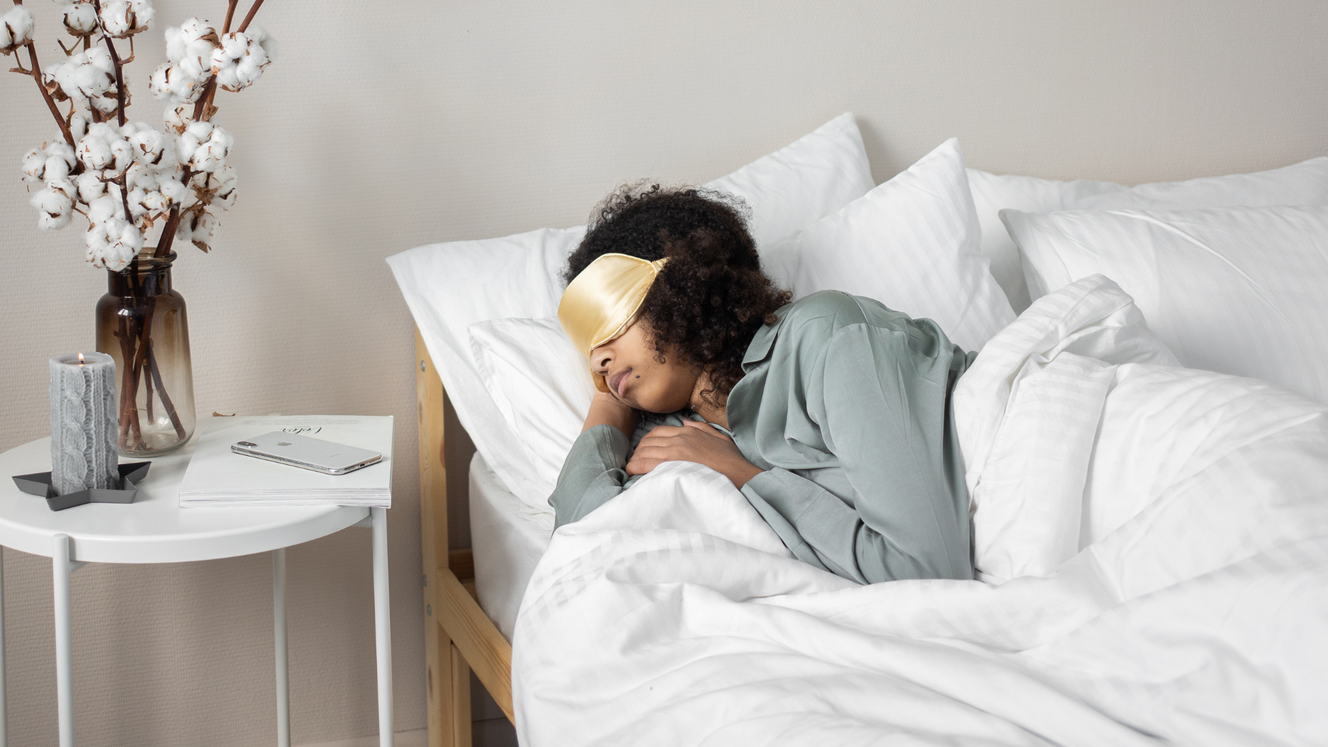 Person sleeping in a white bed beside a small table with flowers and a lamp