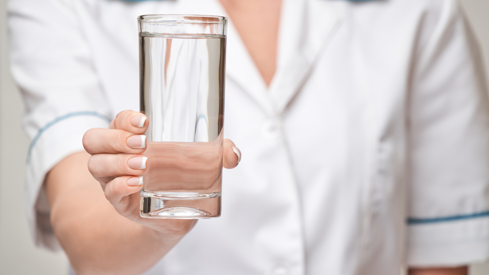 Person in a white shirt holding a clear glass of water toward the camera