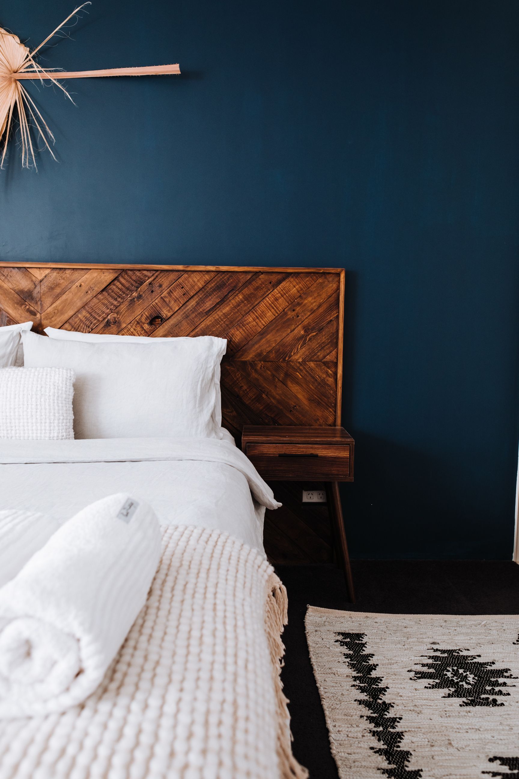 Cozy bedroom with dark blue walls, wooden headboard, white bedding, and a patterned rug