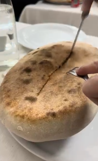Tagliare a mano una sfoglia rotonda e dorata con zucchero a velo su una tovaglia bianca.