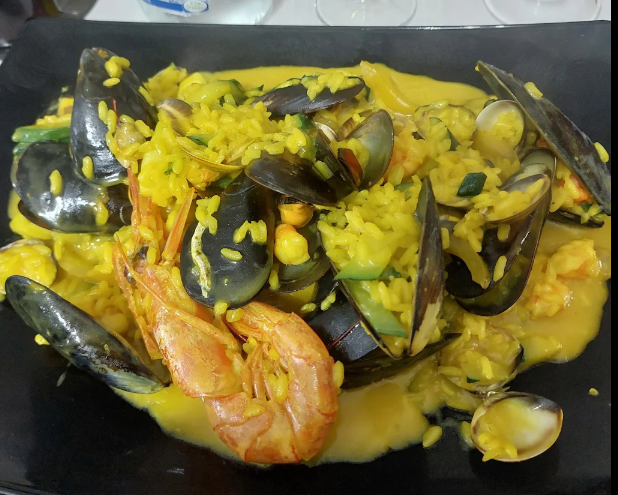 Piatto di pesce con cozze, gamberi e riso in salsa gialla su un piatto nero.