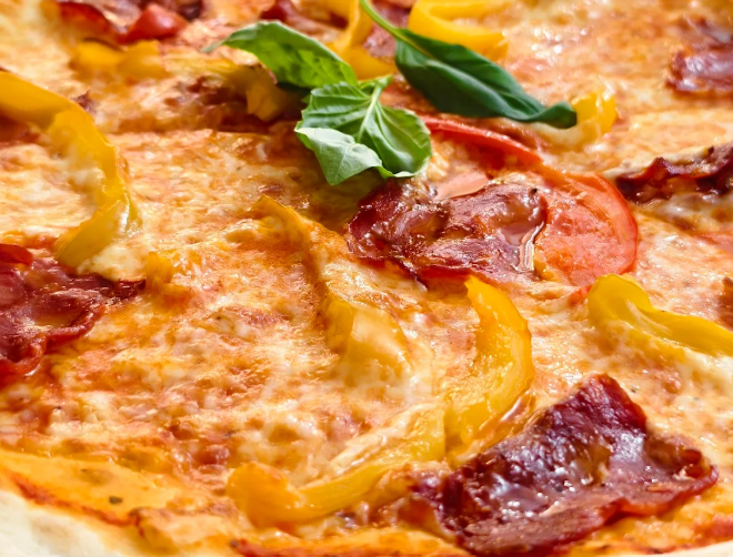 Primo piano di una pizza con peperoni e peperoni gialli, formaggio fuso e foglie di basilico.