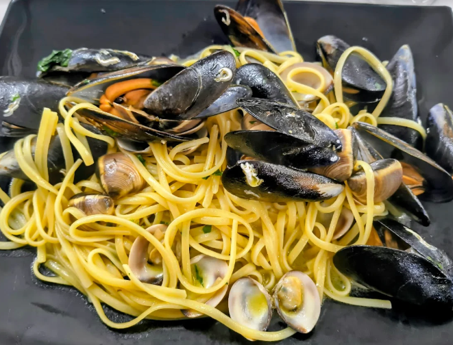 Spaghetti con cozze in una ciotola nera, guarniti con conchiglie di vongole.