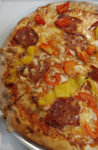 Primo piano di una pizza con formaggio fuso, salame piccante e peperoni rossi e gialli.