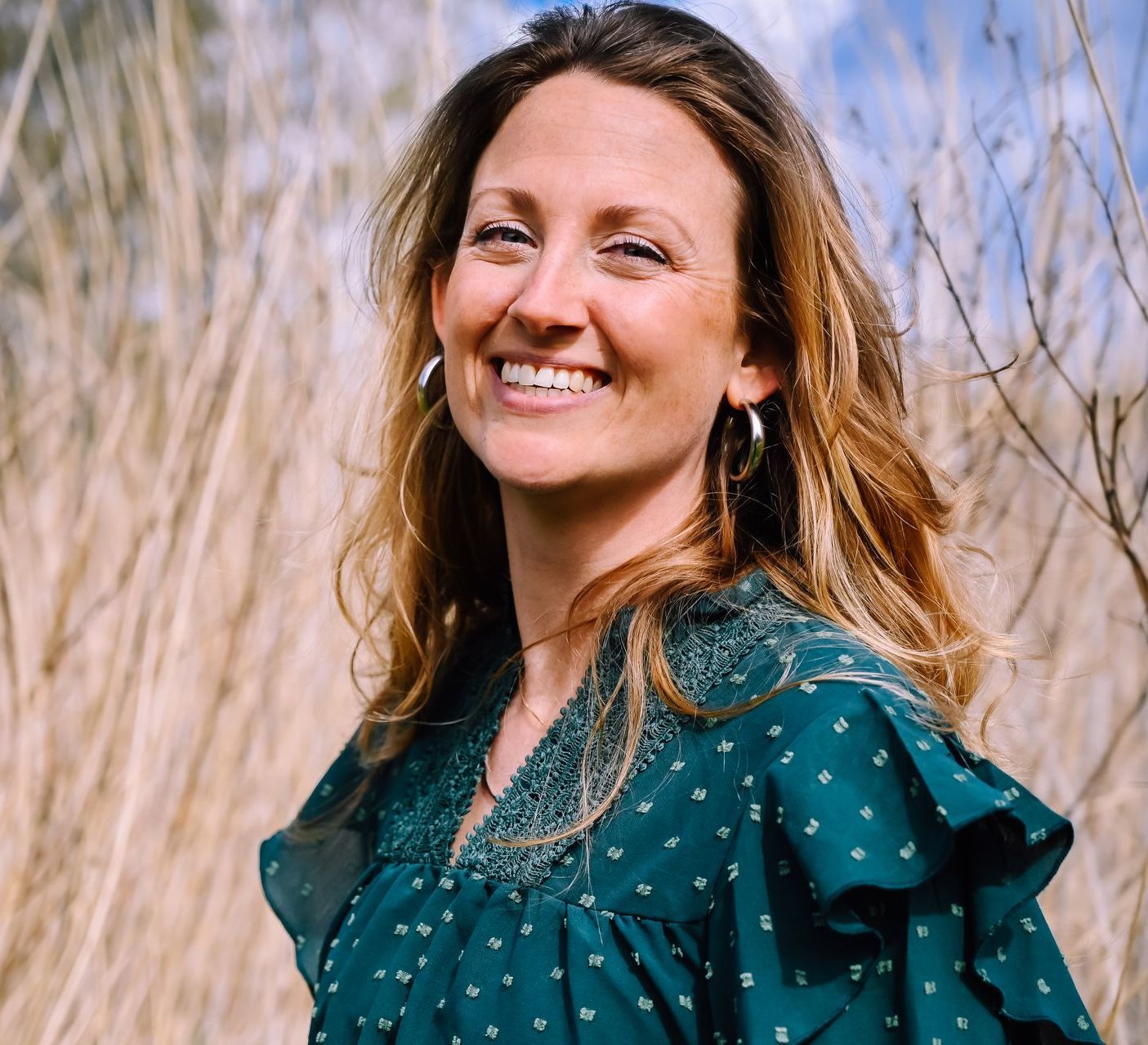 Een vrouw in een groene jurk lacht in een veld met hoog gras.