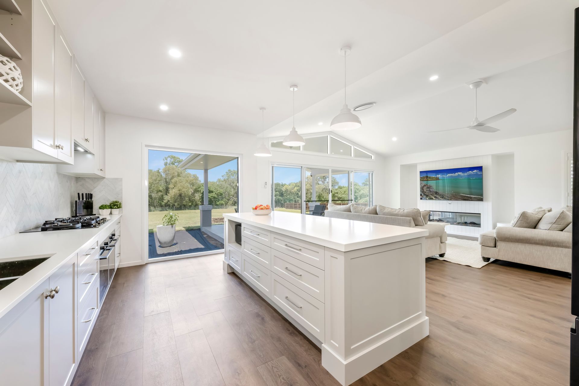 White Kitchen With Island and Open Living Area With Sliding Glass Doors — Master Cabinets Bundaberg in Kensington, QLD