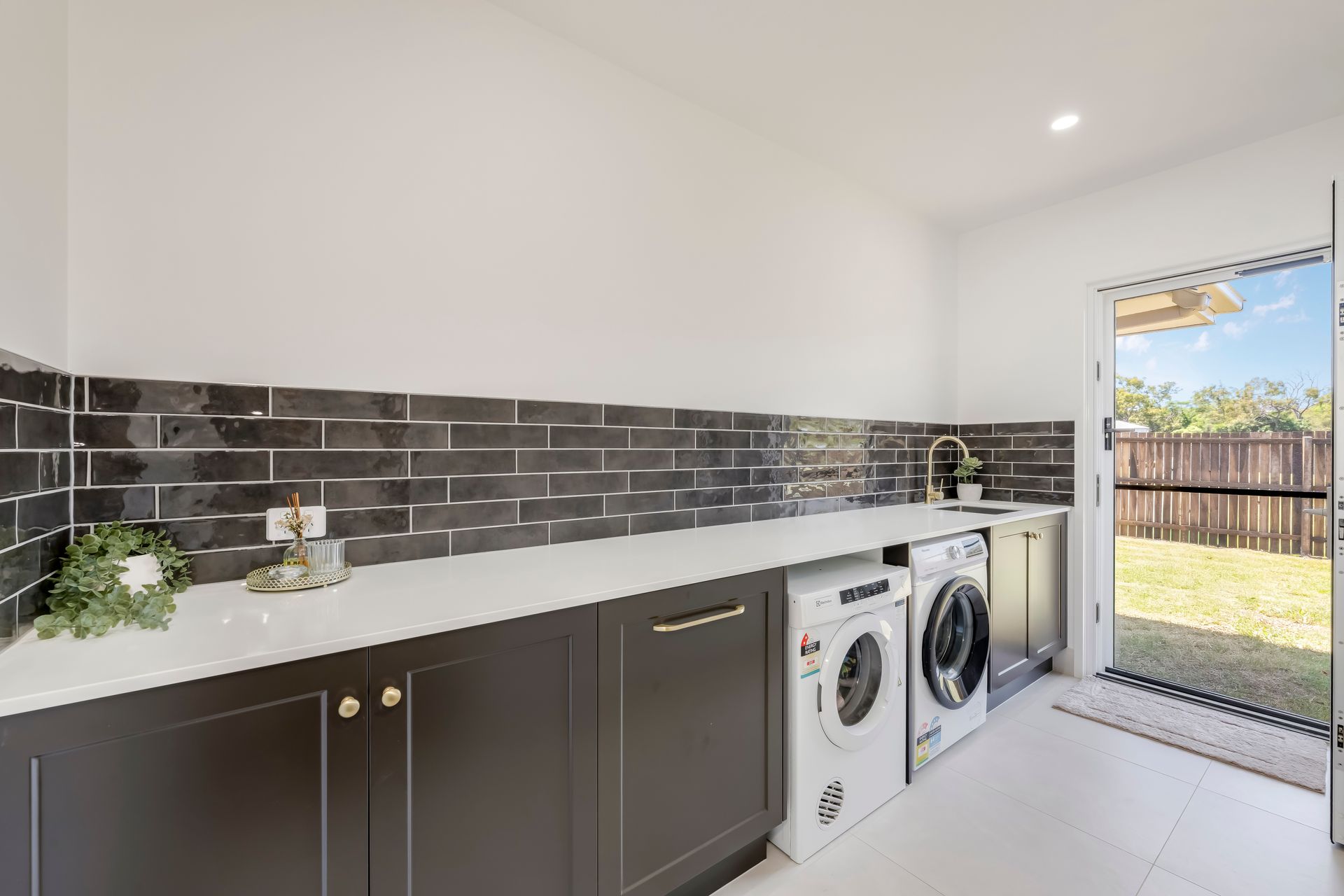 Laundry room with white cabinets, stainless steel sink, wooden shelf, and open door.