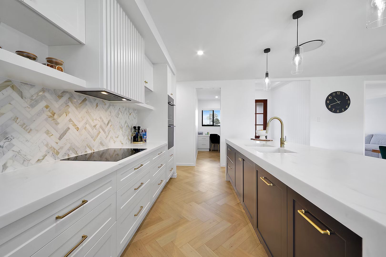 Modern kitchen with white cabinets, gold hardware, and herringbone backsplash. Brown island and wood floors.