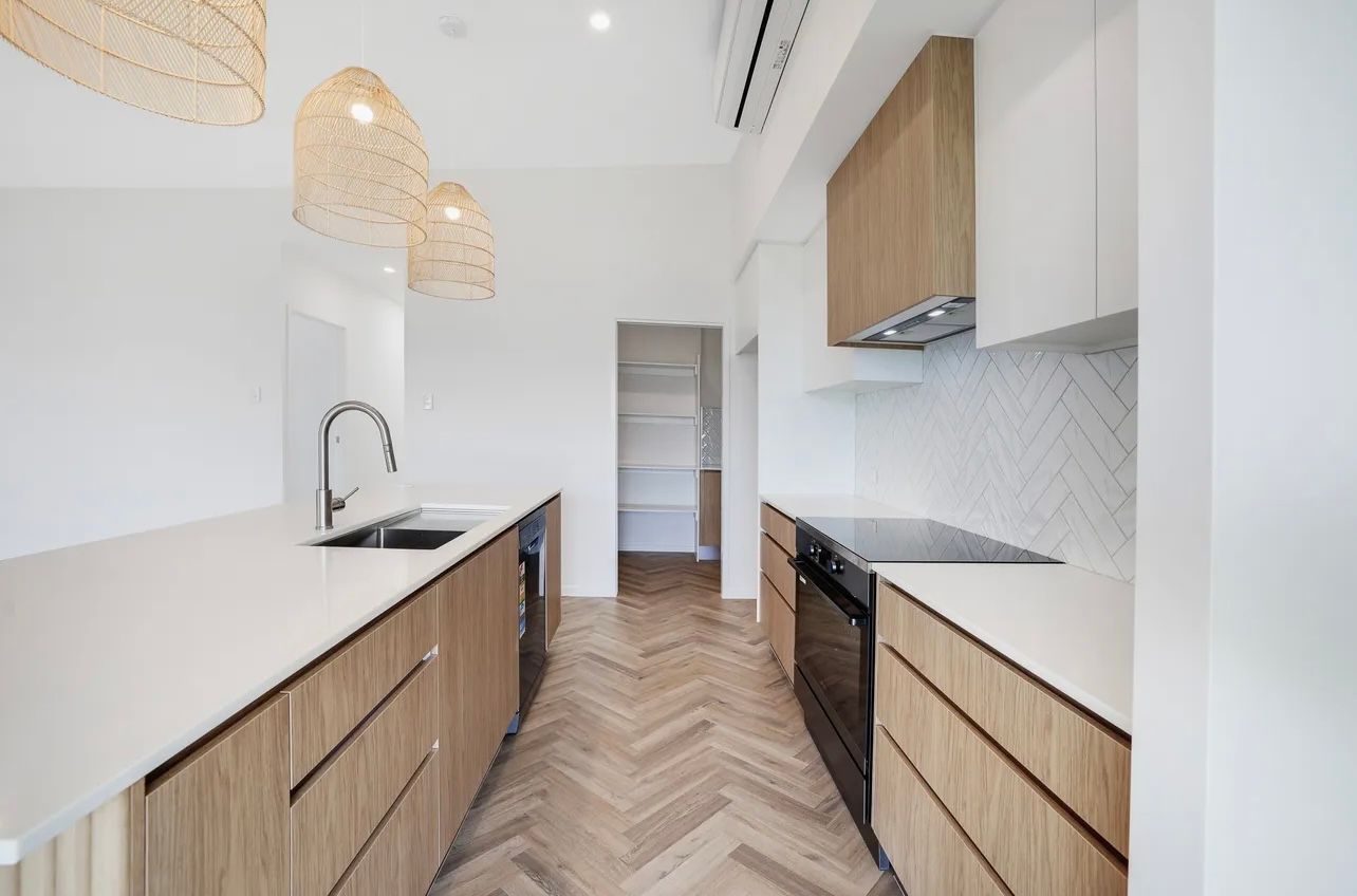Modern kitchen with wooden cabinets, white countertops, and herringbone floors.