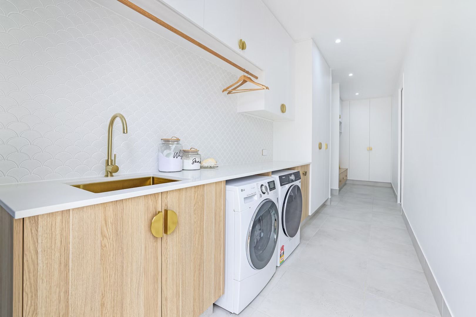 Laundry room with washer and dryer, gold hardware, white and wood cabinetry, and a long hallway.