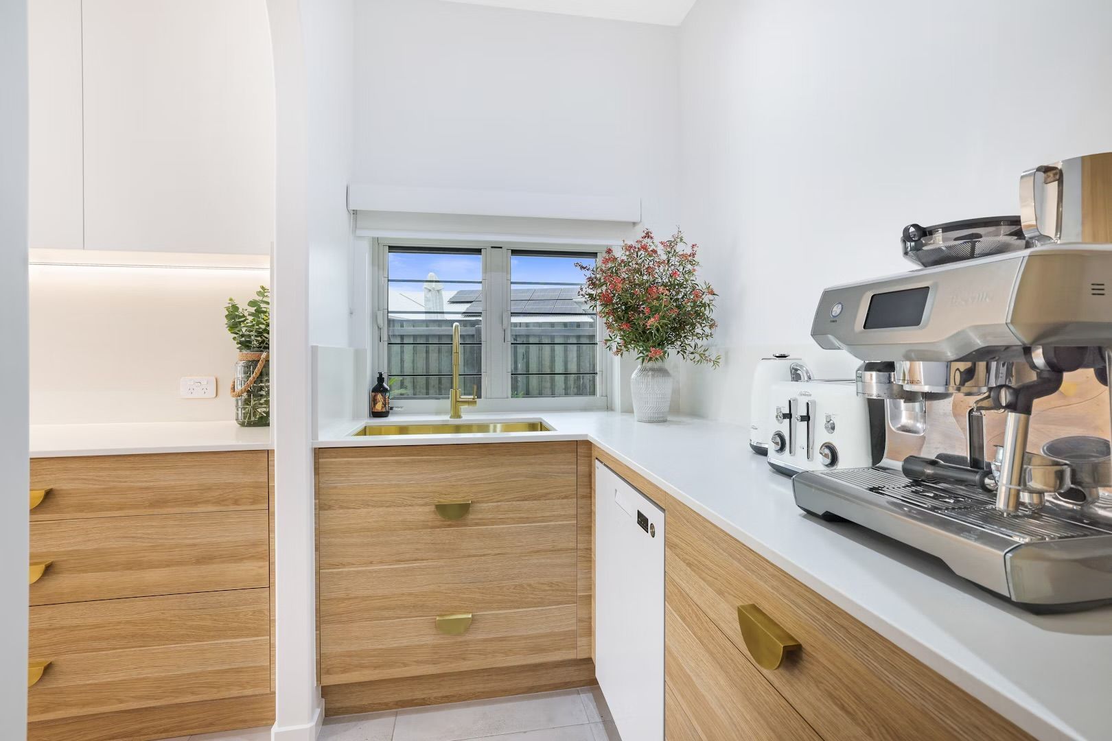 Bright white and wood toned pantry with espresso machine, sink and cabinets.