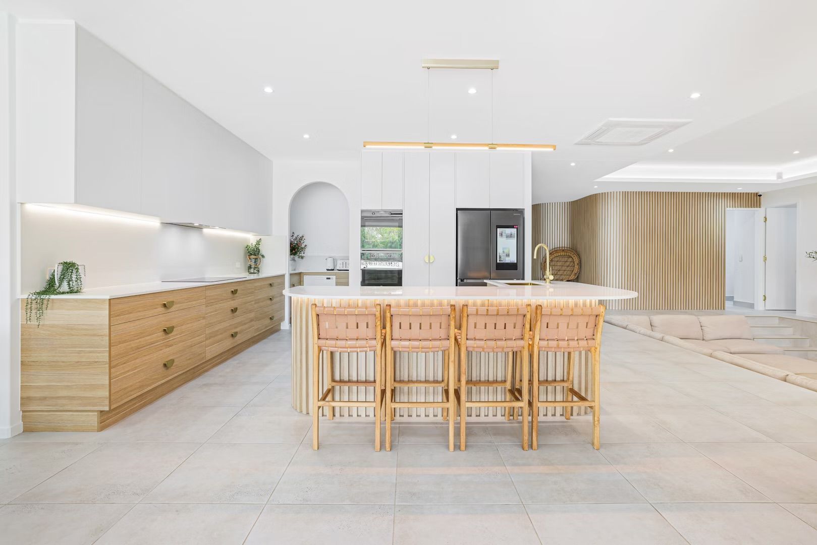 Modern white and wood kitchen with island, seating, and built-in appliances.