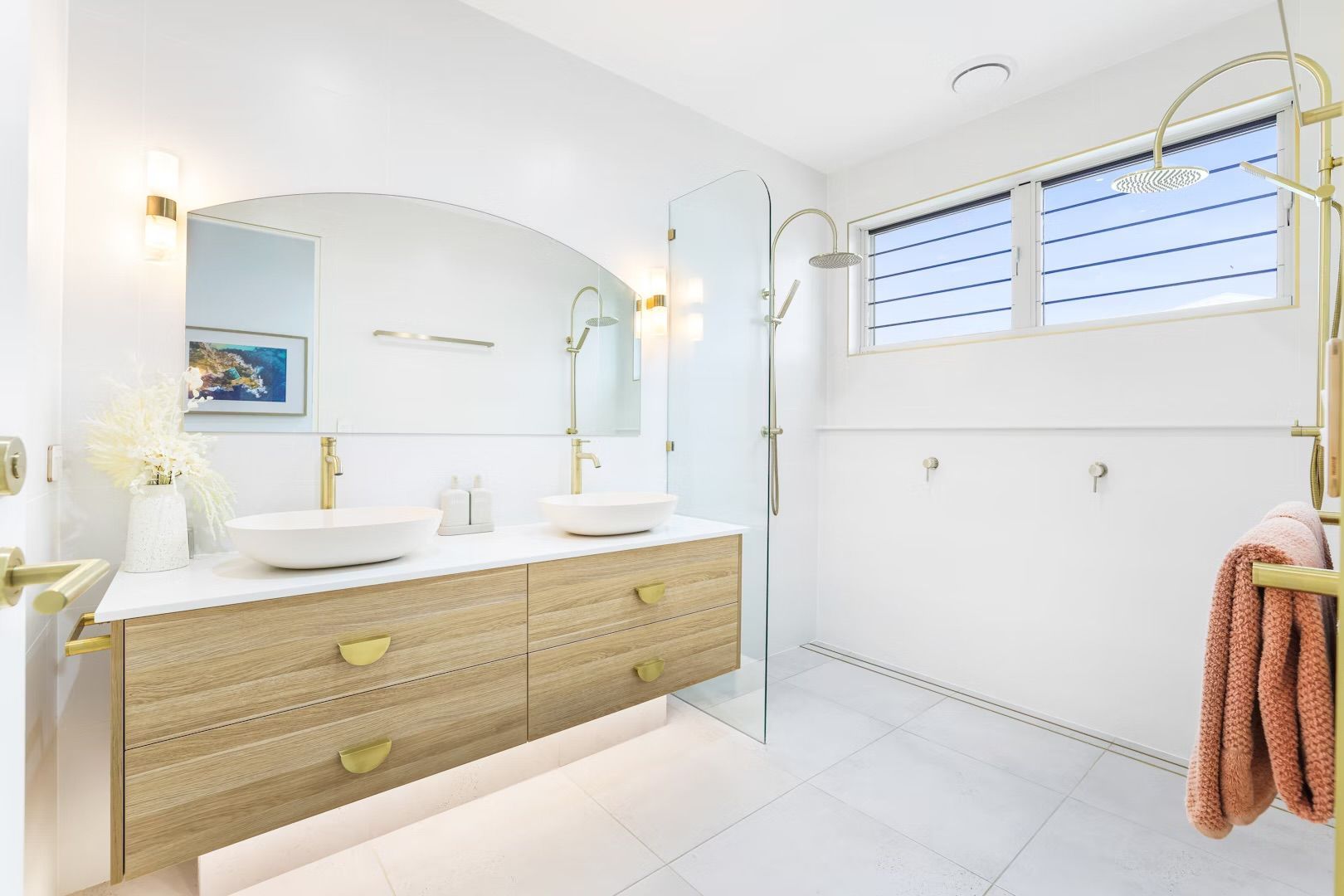 Modern bathroom with white walls, wood vanity, arched mirror, and gold fixtures.