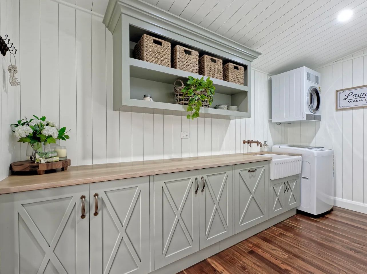 Laundry room with light green cabinets, wood countertop, white washer/dryer, and wicker baskets.
