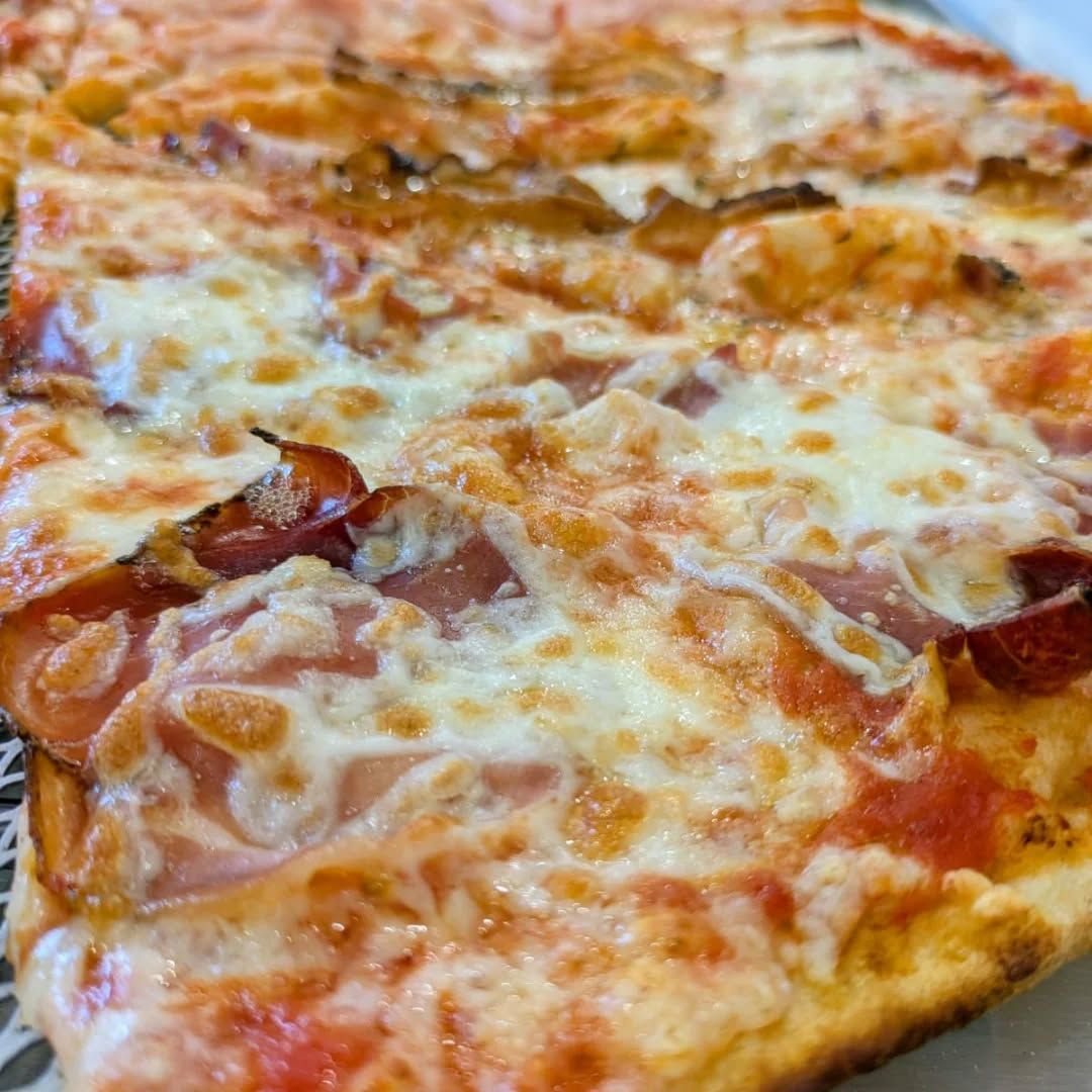 Primo piano di una pizza rettangolare con formaggio, prosciutto e, a volte, pancetta.