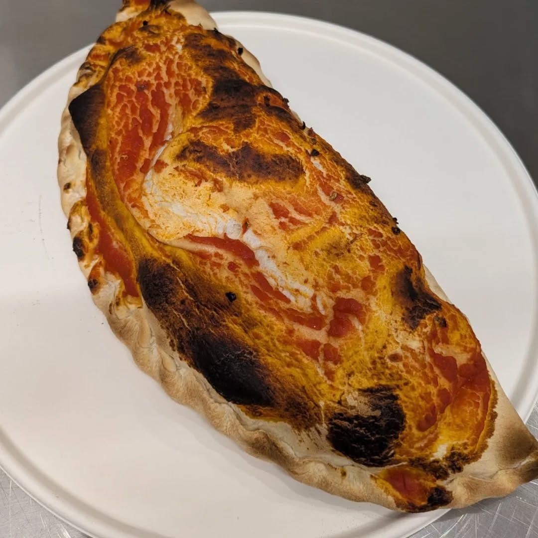 Calzone su un piatto bianco, con una crosta bruciacchiata e bollicina e salsa di pomodoro visibile.