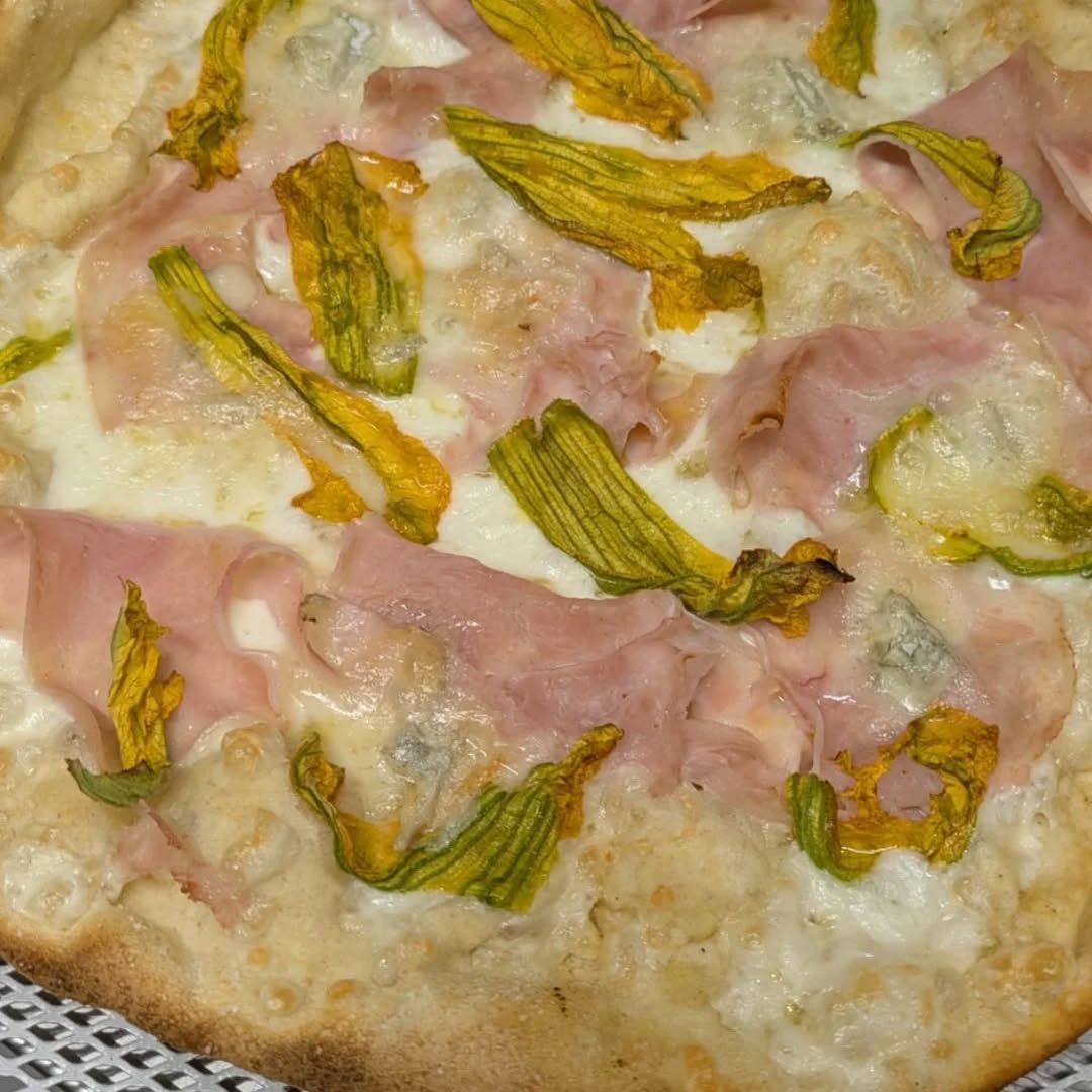 Pizza con prosciutto, fiori di zucca gialli e formaggio blu.