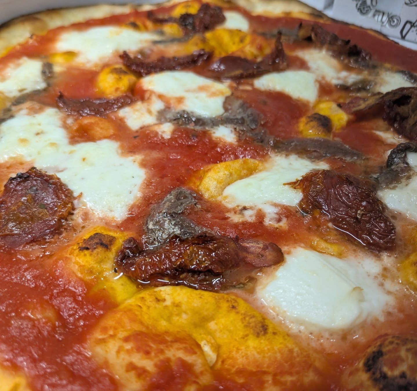 Primo piano di una pizza con salsa rossa, mozzarella e pomodori secchi.