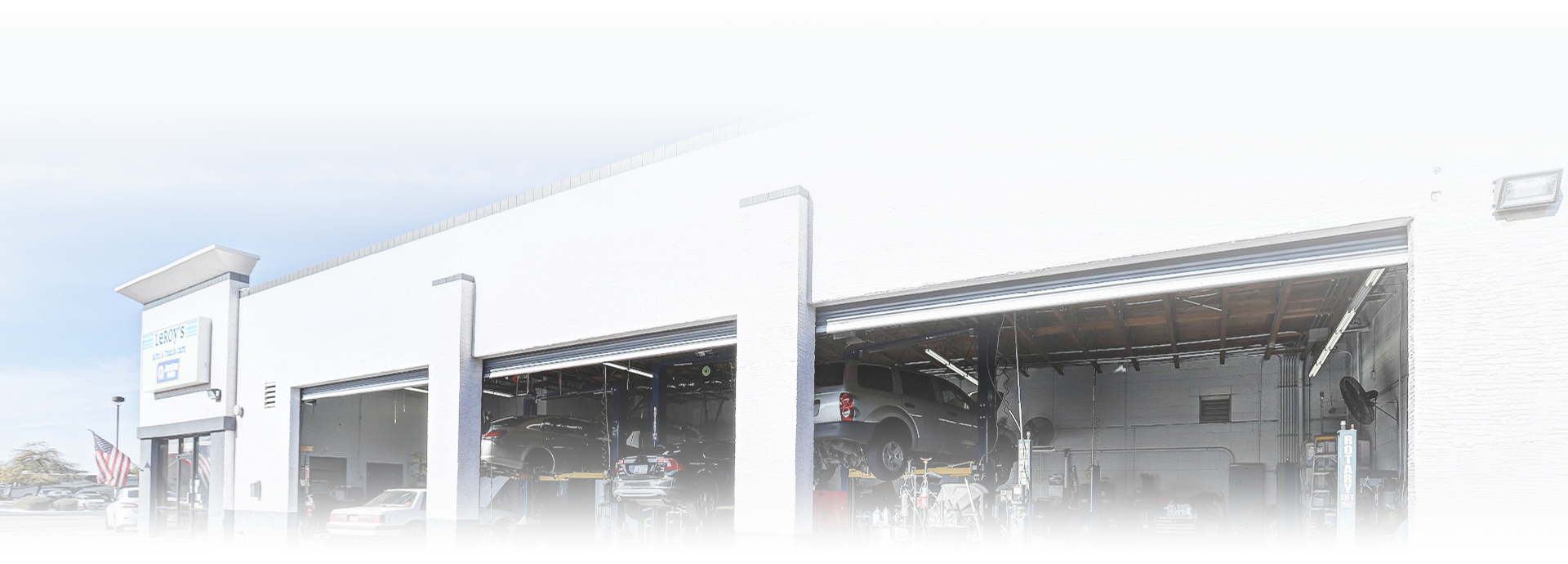 Exterior of a white industrial building with large open garage bays and a covered loading area