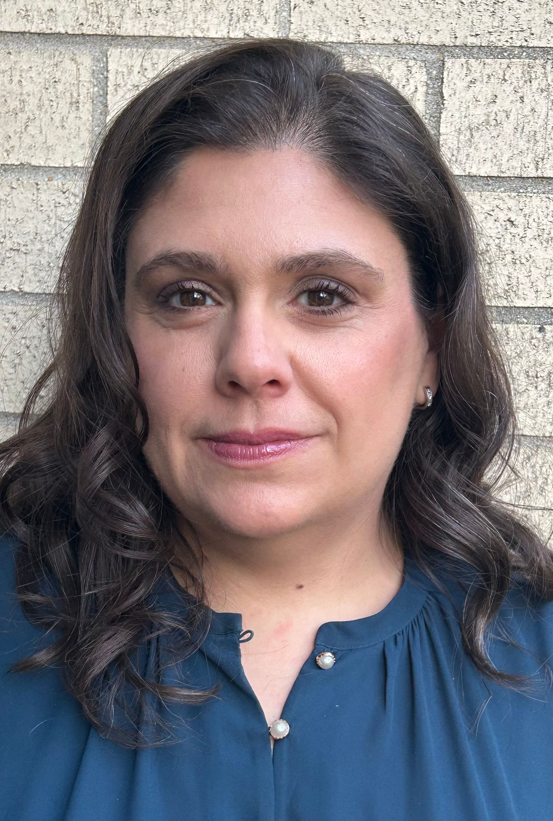 Woman with dark hair in a blue blouse standing before a stone wall