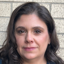 Portrait of a woman with dark hair standing against a light brick wall