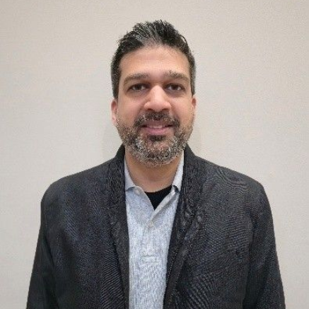 Portrait of a smiling man in a dark jacket and light shirt against a plain beige wall