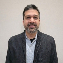 Portrait of a smiling man in a dark blazer and light sweater against a plain wall