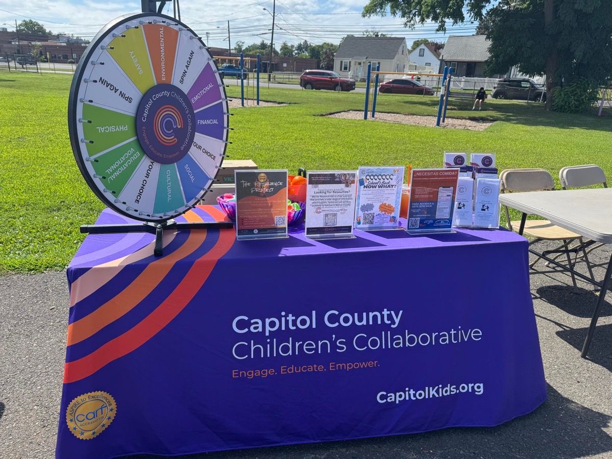 Capitol County Children’s Collaborative booth with purple tablecloth and prize wheel at an outdoor event.