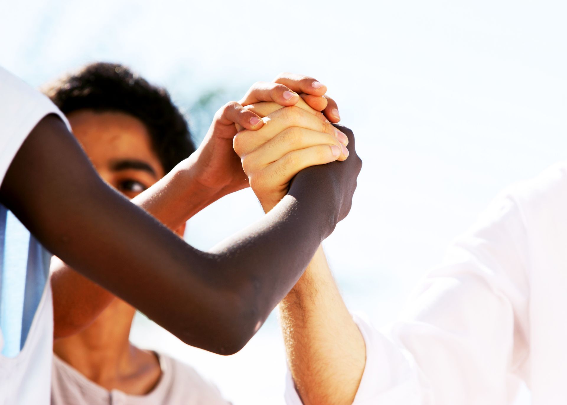 Two people clasp hands in a teamwork gesture against a bright background.