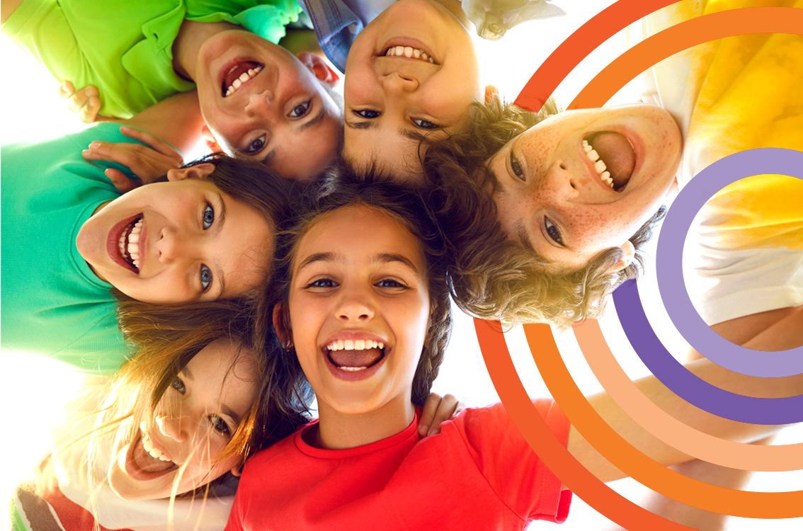 Smiling friends with faces in a circle, looking down toward the camera, with colorful rainbow swirls.