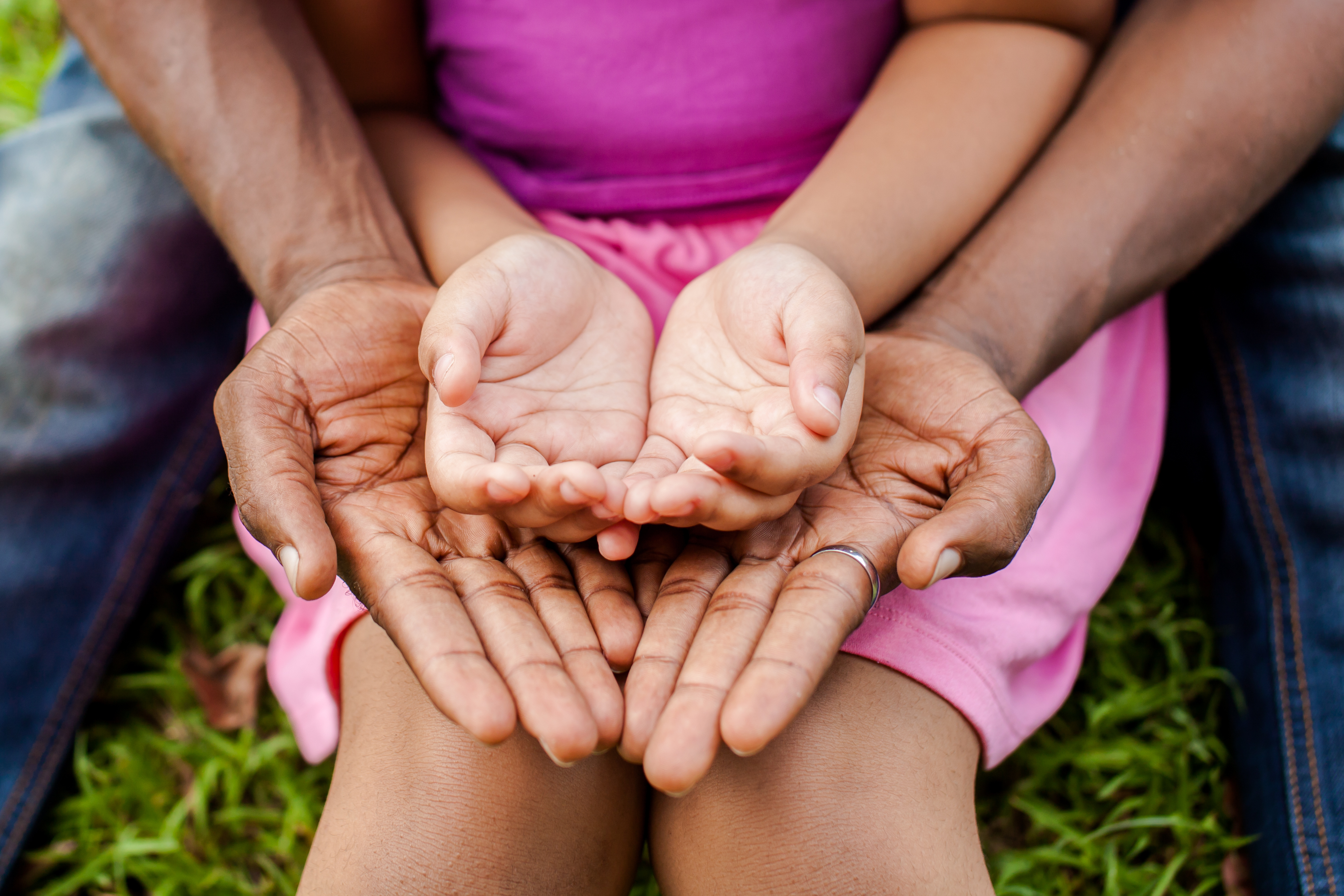 Adult and child hands cupped together over a pink dress in grass