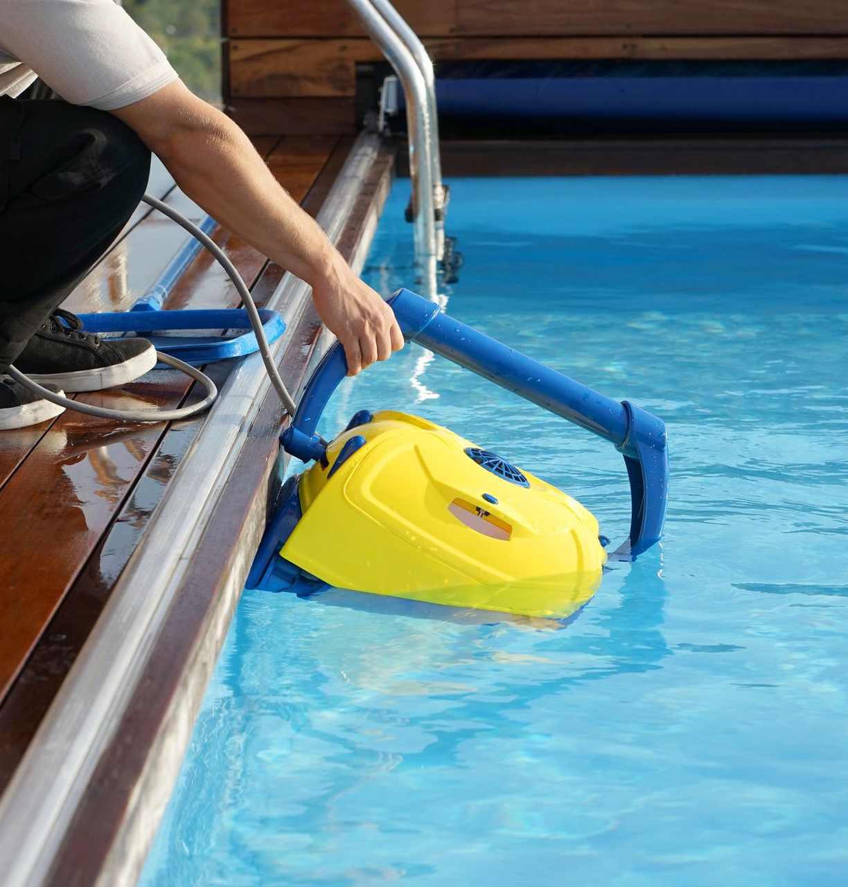 Persona che posiziona un pulitore giallo in una piscina blu.