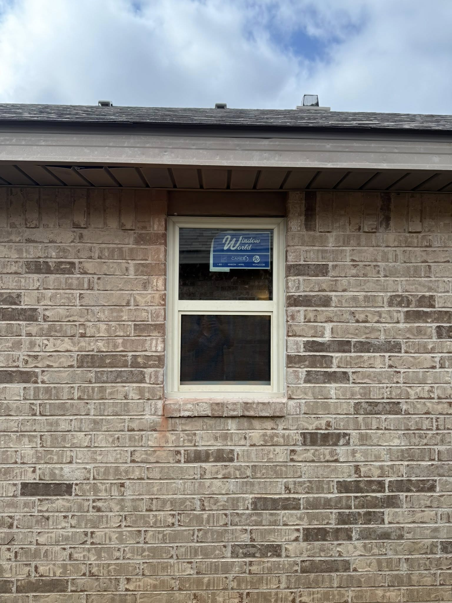 Window in a brick wall under a roof overhang; cloudy sky in the background.