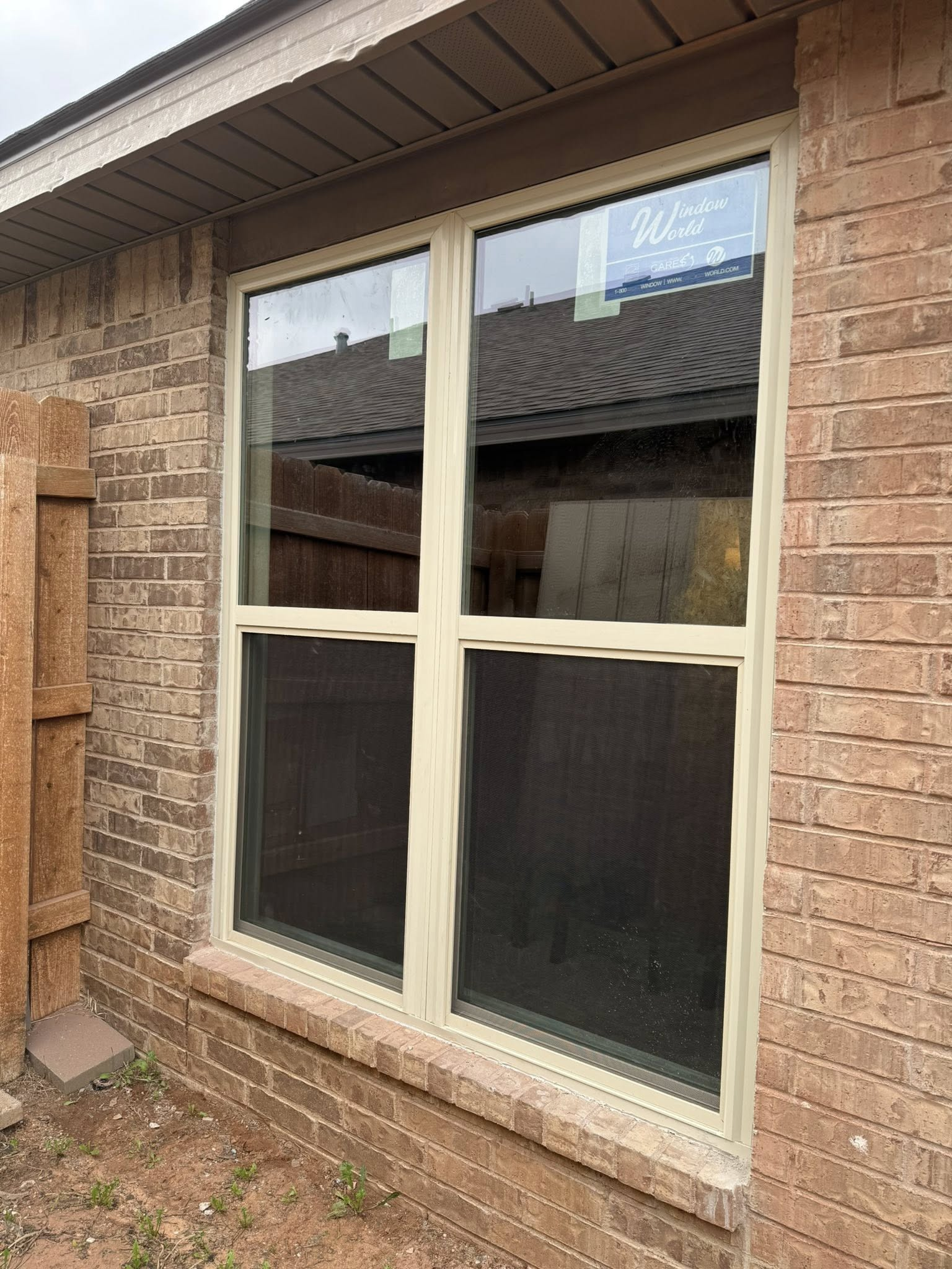 Brick house exterior with a two-panel window, beige frame, and partial view of another building.
