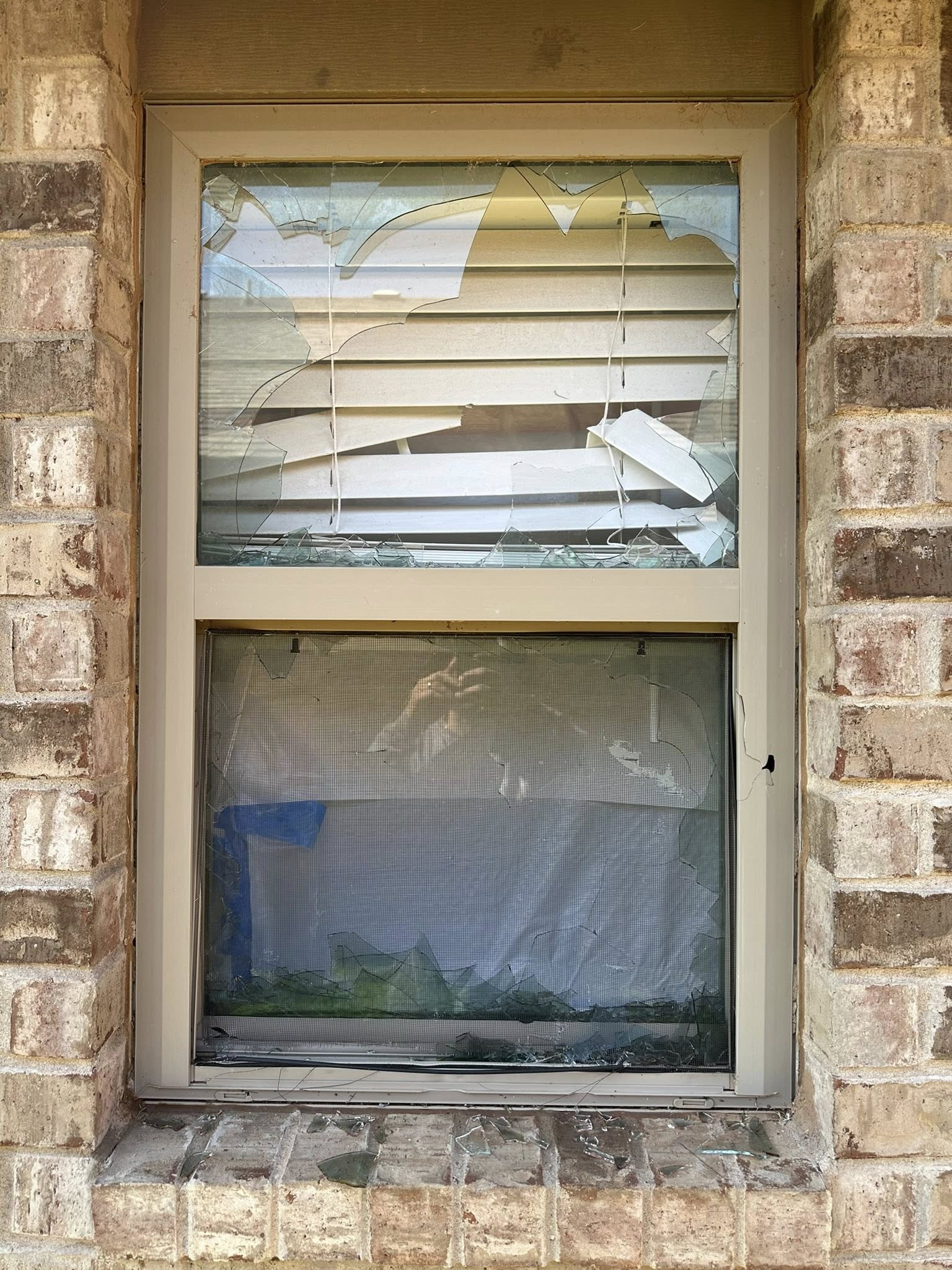 Broken window with damaged blinds and screen. Brick wall.