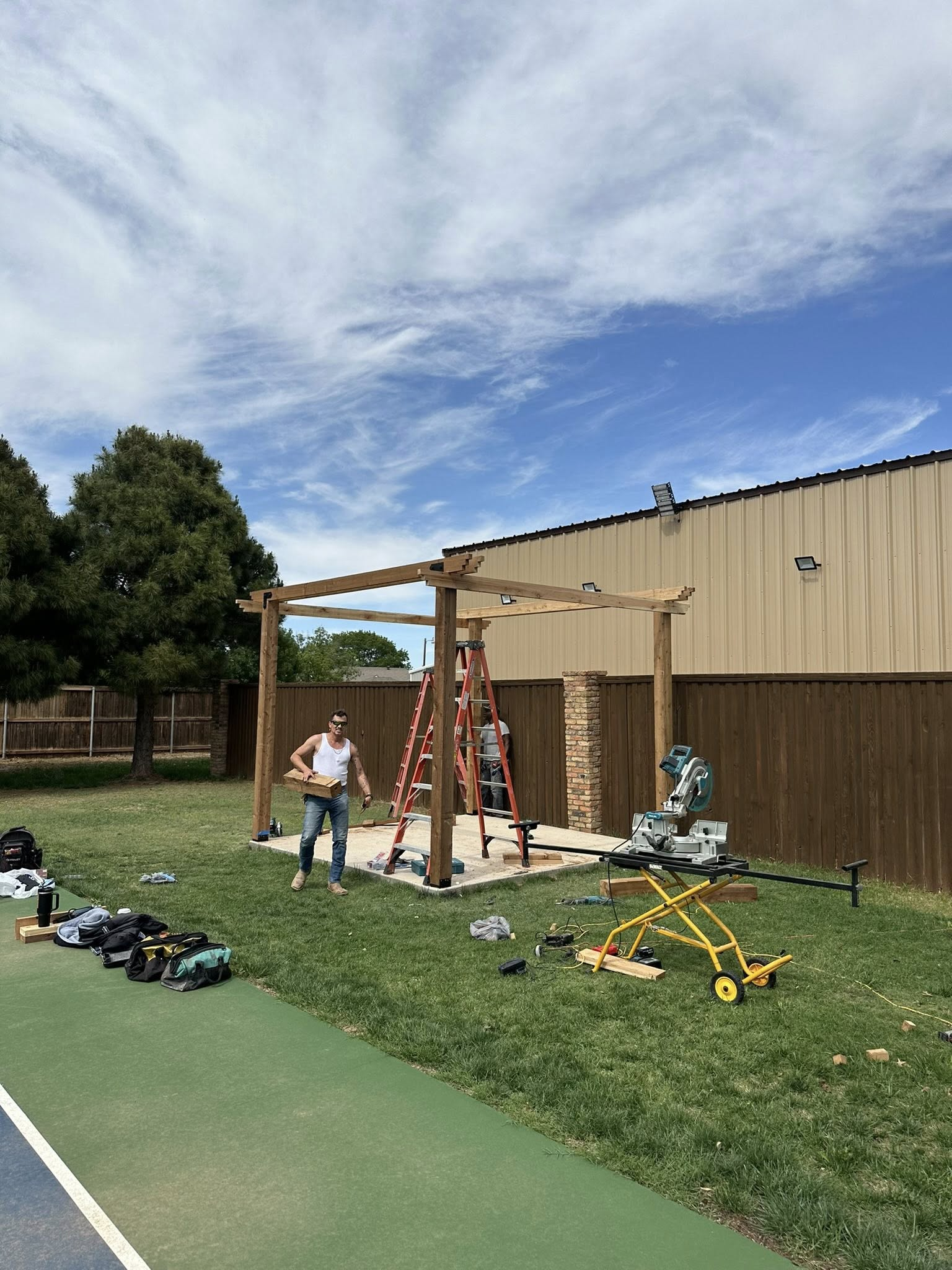 People building a wooden pergola in a backyard on a sunny day.